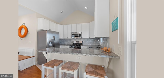 kitchen featuring stainless steel appliances, kitchen peninsula, lofted ceiling, a kitchen bar, and white cabinets