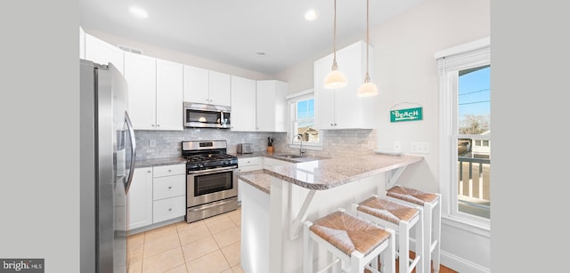 kitchen featuring sink, kitchen peninsula, pendant lighting, white cabinets, and appliances with stainless steel finishes