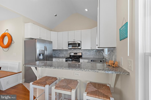 kitchen with kitchen peninsula, stainless steel appliances, sink, white cabinetry, and lofted ceiling