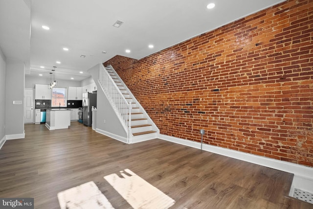 unfurnished living room featuring a chandelier, hardwood / wood-style floors, brick wall, and sink