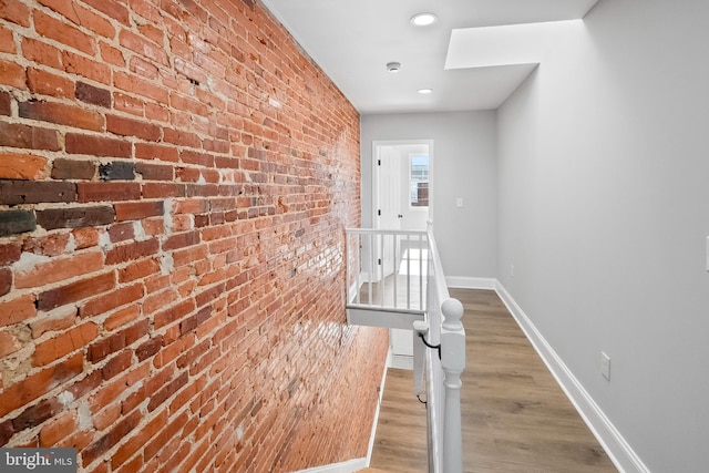 hall featuring wood-type flooring and brick wall