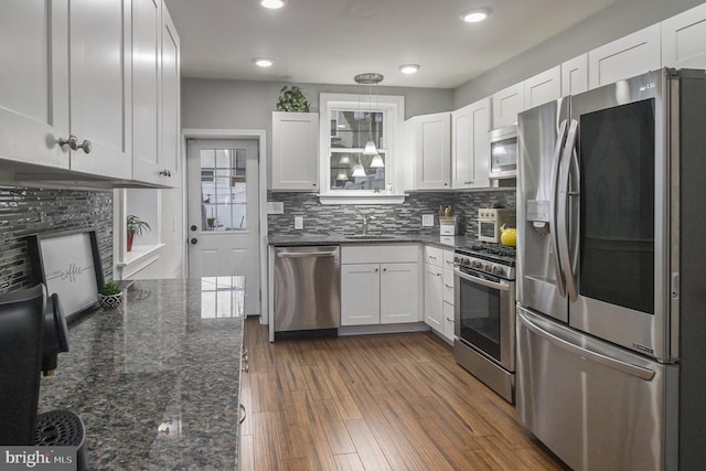 kitchen featuring white cabinetry, dark wood-type flooring, stainless steel appliances, dark stone countertops, and decorative backsplash