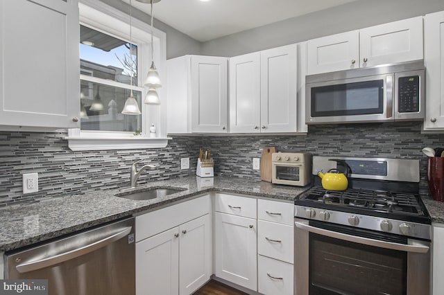 kitchen featuring pendant lighting, backsplash, white cabinets, sink, and appliances with stainless steel finishes