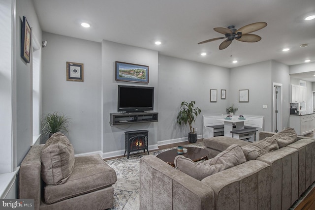 living room with a wood stove, ceiling fan, and wood-type flooring