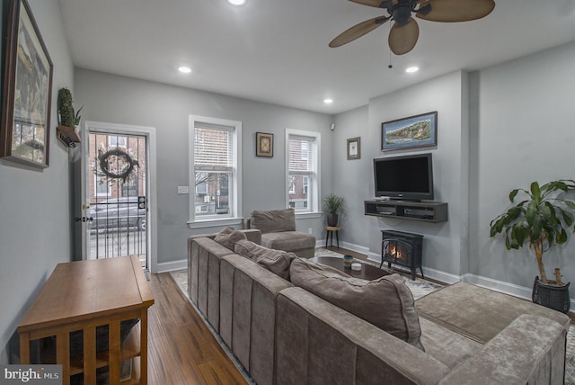 living room with a wood stove, ceiling fan, and dark wood-type flooring