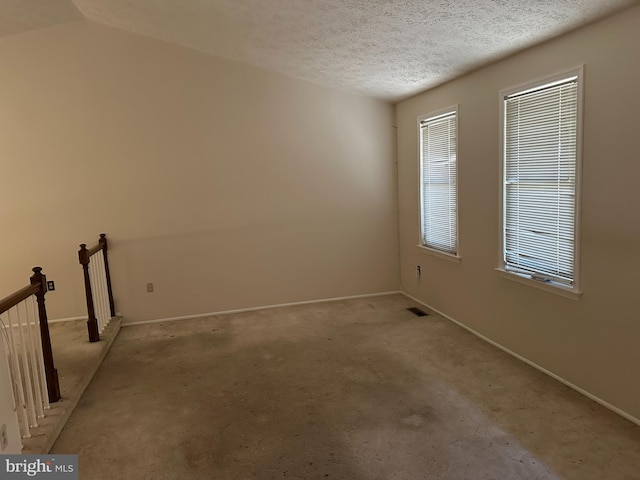 carpeted empty room with plenty of natural light, a textured ceiling, and vaulted ceiling