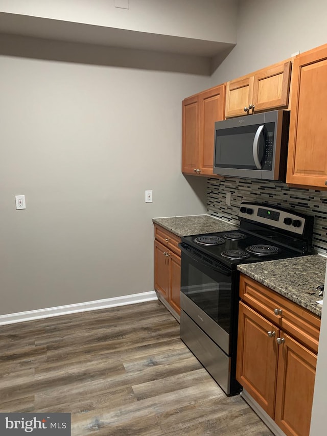 kitchen with backsplash, dark stone countertops, hardwood / wood-style flooring, and appliances with stainless steel finishes