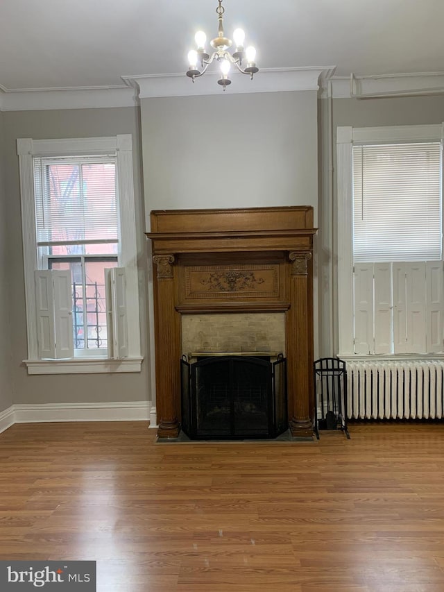 unfurnished living room featuring hardwood / wood-style floors, a notable chandelier, radiator heating unit, and ornamental molding