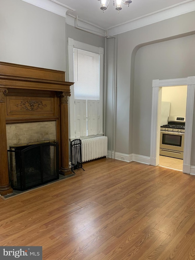 unfurnished living room featuring a notable chandelier, light wood-type flooring, radiator heating unit, and ornamental molding