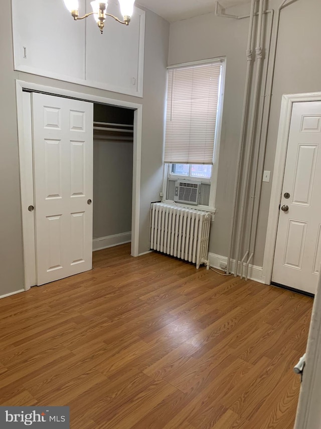 unfurnished bedroom with radiator heating unit, an inviting chandelier, cooling unit, a closet, and hardwood / wood-style flooring