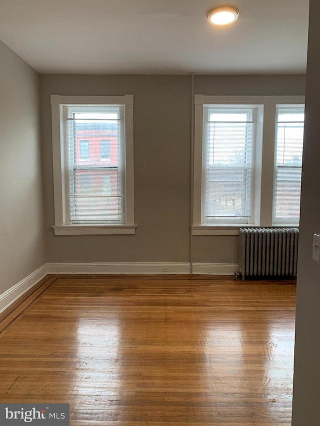 empty room featuring radiator heating unit, hardwood / wood-style flooring, and a healthy amount of sunlight