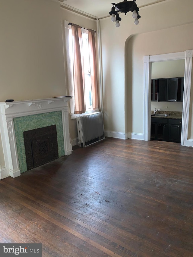 unfurnished living room featuring dark hardwood / wood-style floors, radiator, and sink