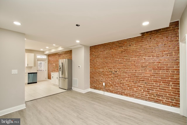 unfurnished living room featuring light hardwood / wood-style flooring and brick wall