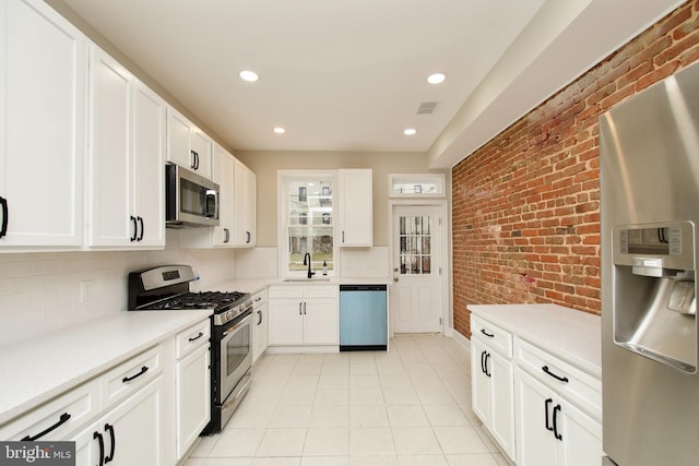 kitchen featuring backsplash, brick wall, stainless steel appliances, sink, and white cabinets