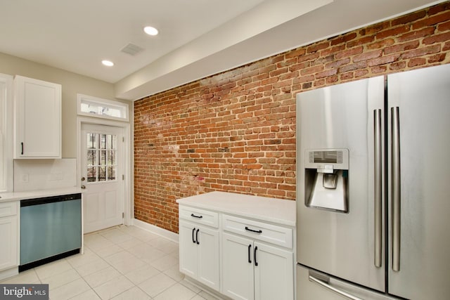 kitchen featuring light tile patterned floors, white cabinets, stainless steel appliances, and brick wall