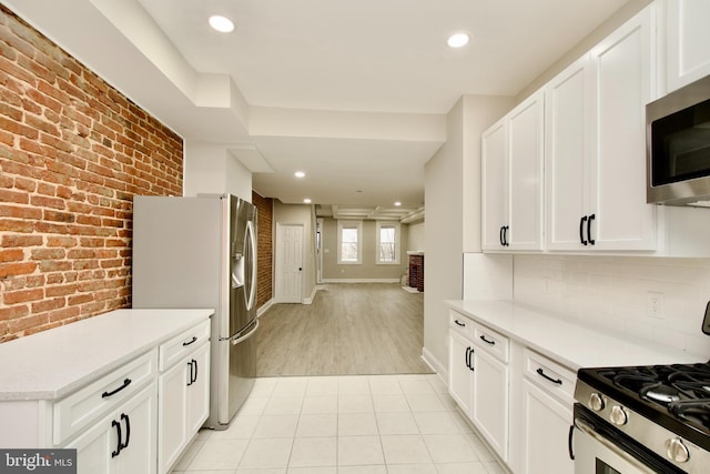 kitchen with white cabinets, stainless steel appliances, and brick wall