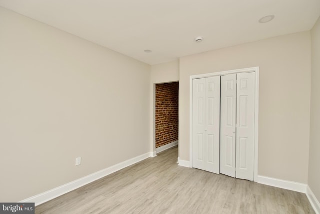 unfurnished bedroom with a closet, brick wall, and light wood-type flooring