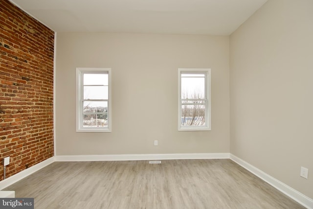 empty room with light wood-type flooring and brick wall