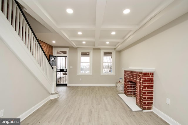 unfurnished living room featuring beamed ceiling, coffered ceiling, a brick fireplace, and light hardwood / wood-style flooring