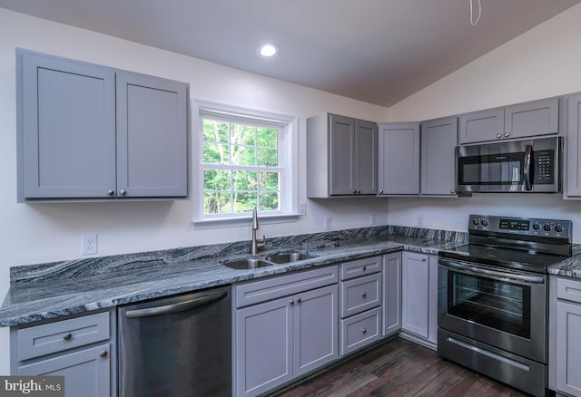 kitchen with dark stone counters, stainless steel appliances, vaulted ceiling, sink, and dark hardwood / wood-style floors