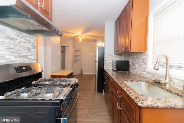 kitchen with light stone countertops, sink, stainless steel appliances, light hardwood / wood-style flooring, and backsplash