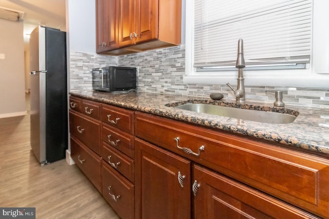 kitchen with stone counters, sink, tasteful backsplash, stainless steel fridge, and light hardwood / wood-style floors