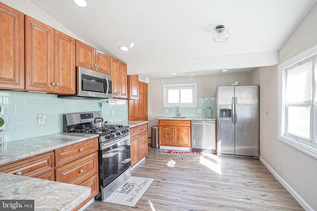 kitchen with backsplash, vaulted ceiling, stainless steel appliances, and light hardwood / wood-style flooring