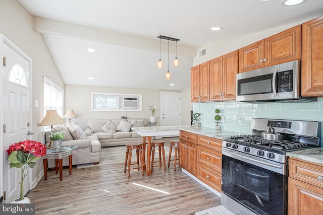 kitchen with decorative backsplash, appliances with stainless steel finishes, vaulted ceiling, pendant lighting, and light hardwood / wood-style flooring