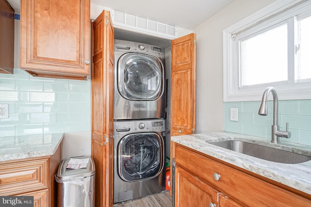 clothes washing area with sink, stacked washer and dryer, and hardwood / wood-style flooring