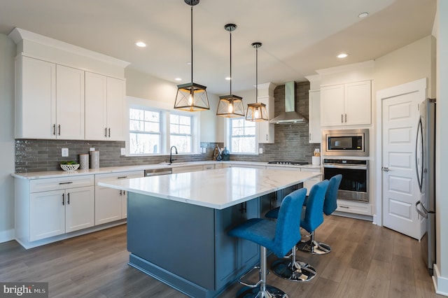 kitchen with wall chimney exhaust hood, appliances with stainless steel finishes, a kitchen island, and white cabinets