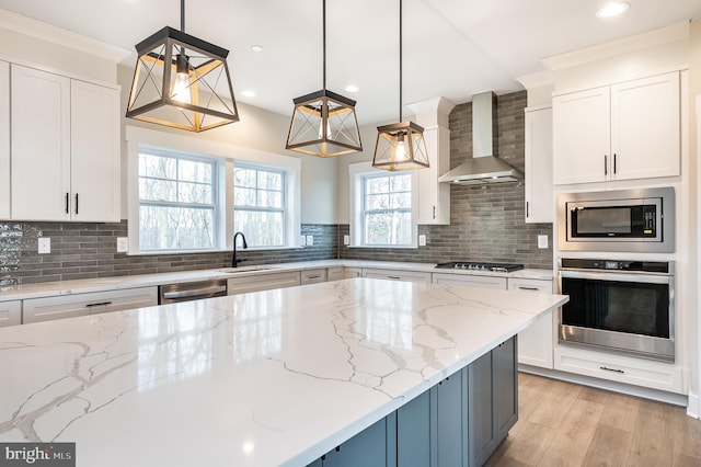 kitchen with appliances with stainless steel finishes, pendant lighting, sink, light stone counters, and wall chimney range hood