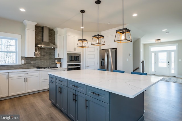 kitchen with white cabinets, decorative light fixtures, wall chimney exhaust hood, and appliances with stainless steel finishes