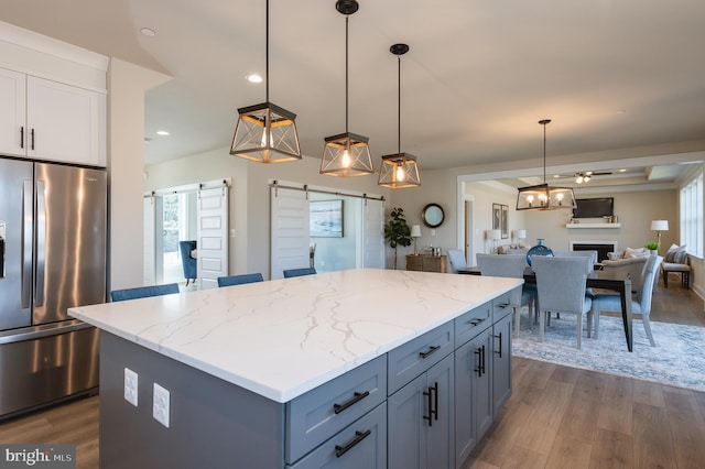 kitchen featuring dark wood-type flooring, stainless steel refrigerator with ice dispenser, a kitchen island, decorative light fixtures, and a barn door