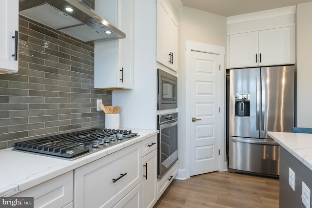 kitchen featuring white cabinets, light stone countertops, wall chimney exhaust hood, and appliances with stainless steel finishes