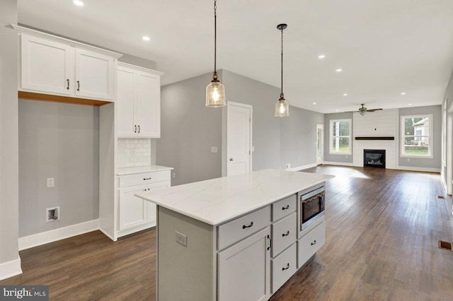 kitchen with white cabinetry, stainless steel microwave, light stone countertops, and decorative light fixtures