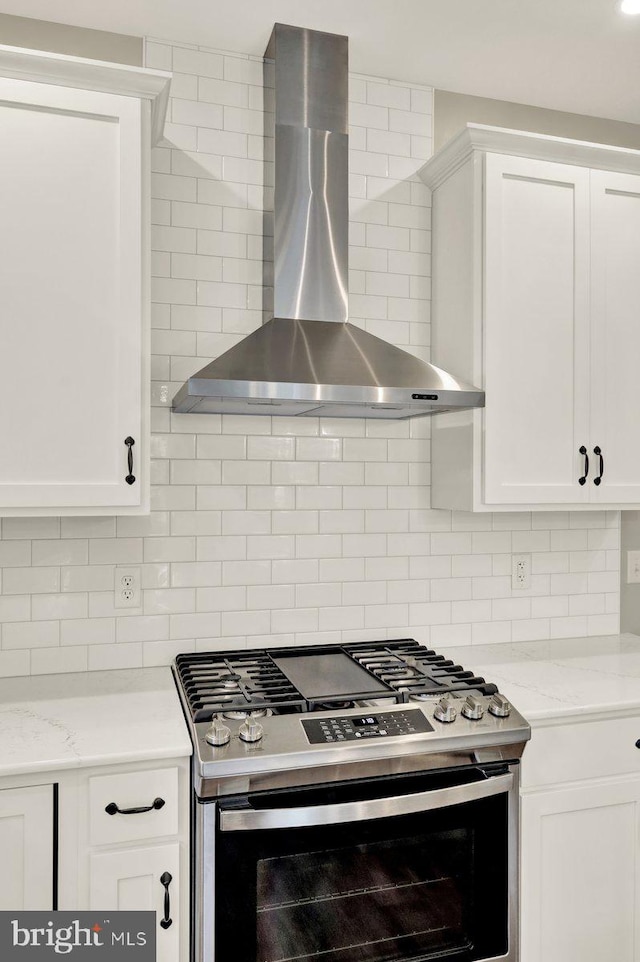 kitchen featuring wall chimney exhaust hood, stainless steel gas range oven, decorative backsplash, and white cabinetry