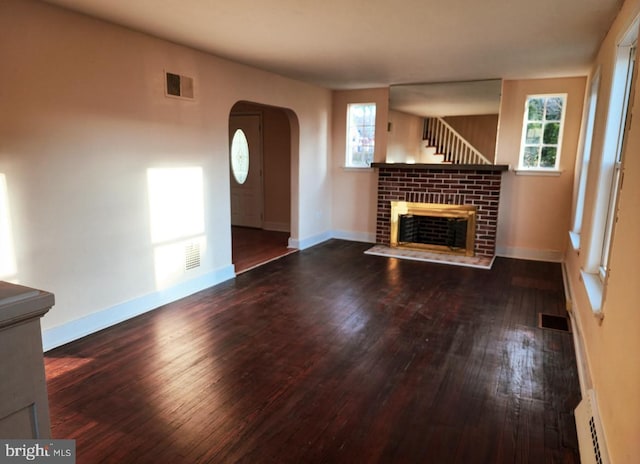 unfurnished living room featuring a baseboard heating unit, a brick fireplace, and dark wood-type flooring