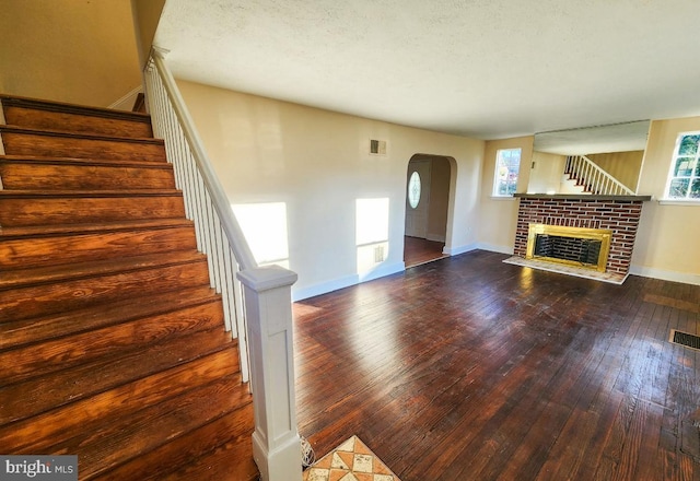 unfurnished living room with hardwood / wood-style floors, a textured ceiling, a brick fireplace, and plenty of natural light