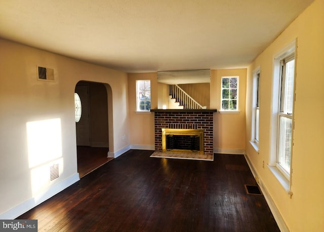 unfurnished living room with a wealth of natural light, dark wood-type flooring, and a brick fireplace