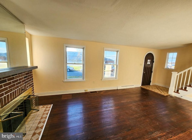 unfurnished living room featuring a healthy amount of sunlight, dark hardwood / wood-style floors, and a brick fireplace