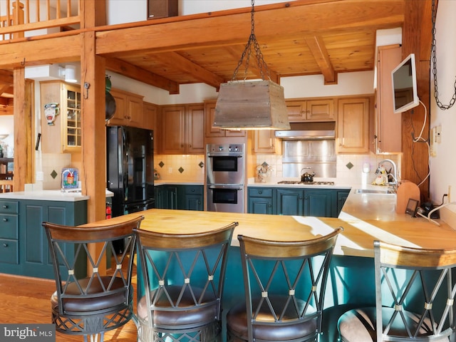 kitchen with stainless steel double oven, extractor fan, black fridge, decorative light fixtures, and wall chimney exhaust hood