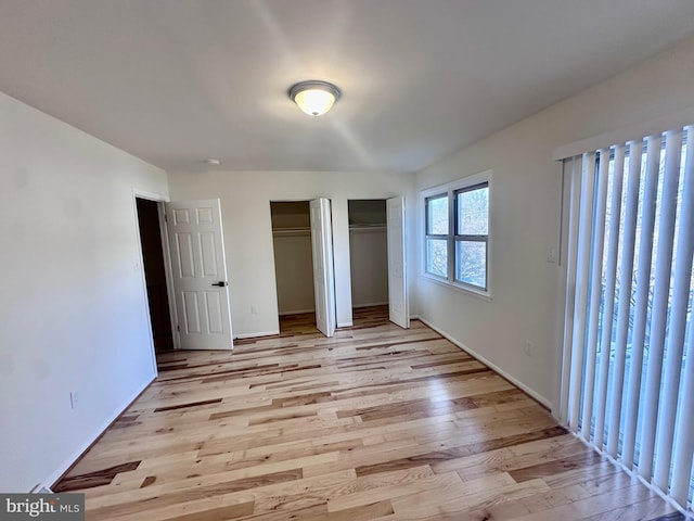 unfurnished bedroom featuring multiple closets and light wood-type flooring