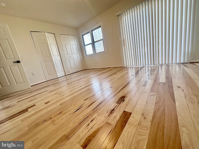 unfurnished bedroom featuring multiple closets and light hardwood / wood-style floors