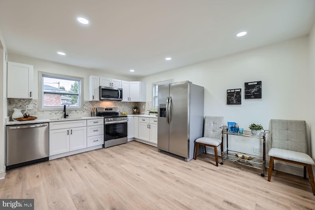 kitchen featuring white cabinetry, sink, stainless steel appliances, light hardwood / wood-style floors, and decorative backsplash