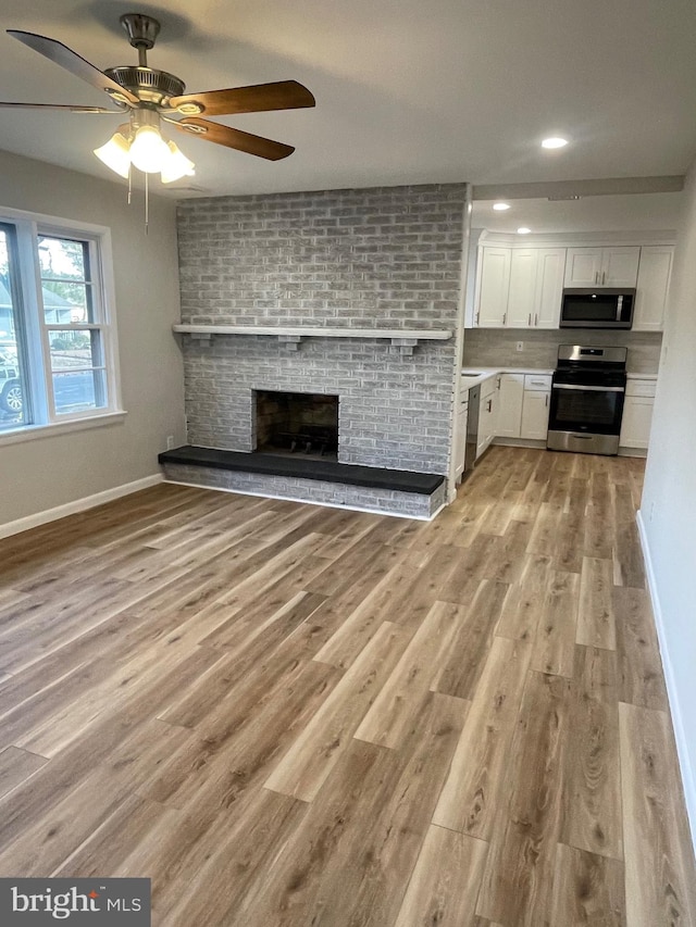 interior space featuring a brick fireplace, white cabinetry, appliances with stainless steel finishes, and light hardwood / wood-style flooring