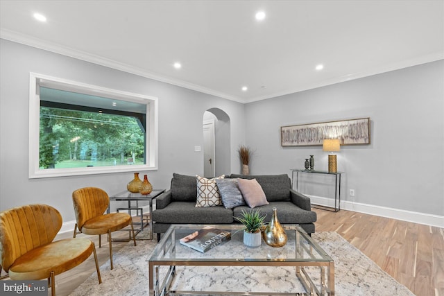 living area featuring arched walkways, baseboards, crown molding, and light wood-style floors