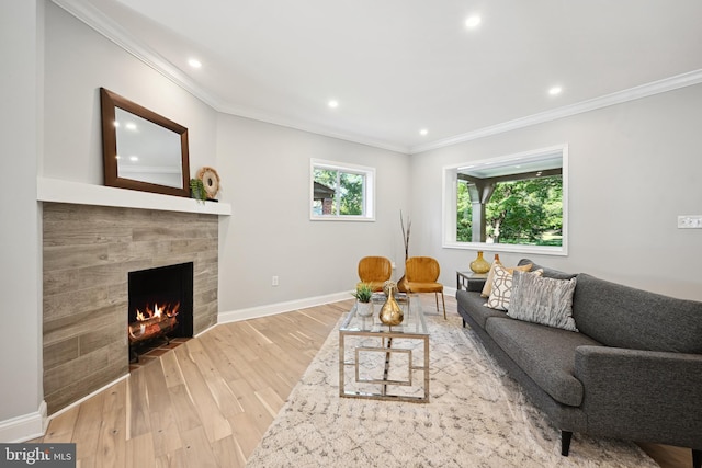 living area with a tiled fireplace, ornamental molding, and wood finished floors