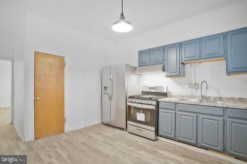 kitchen with pendant lighting, sink, stainless steel gas range, white fridge with ice dispenser, and light hardwood / wood-style floors