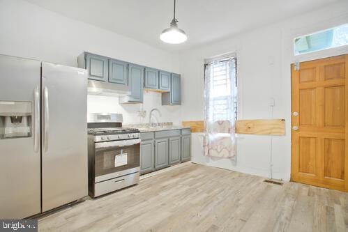 kitchen featuring stainless steel gas range, sink, white refrigerator with ice dispenser, light hardwood / wood-style floors, and hanging light fixtures