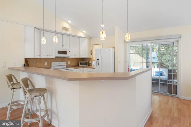 kitchen with a breakfast bar, lofted ceiling, white appliances, kitchen peninsula, and white cabinetry